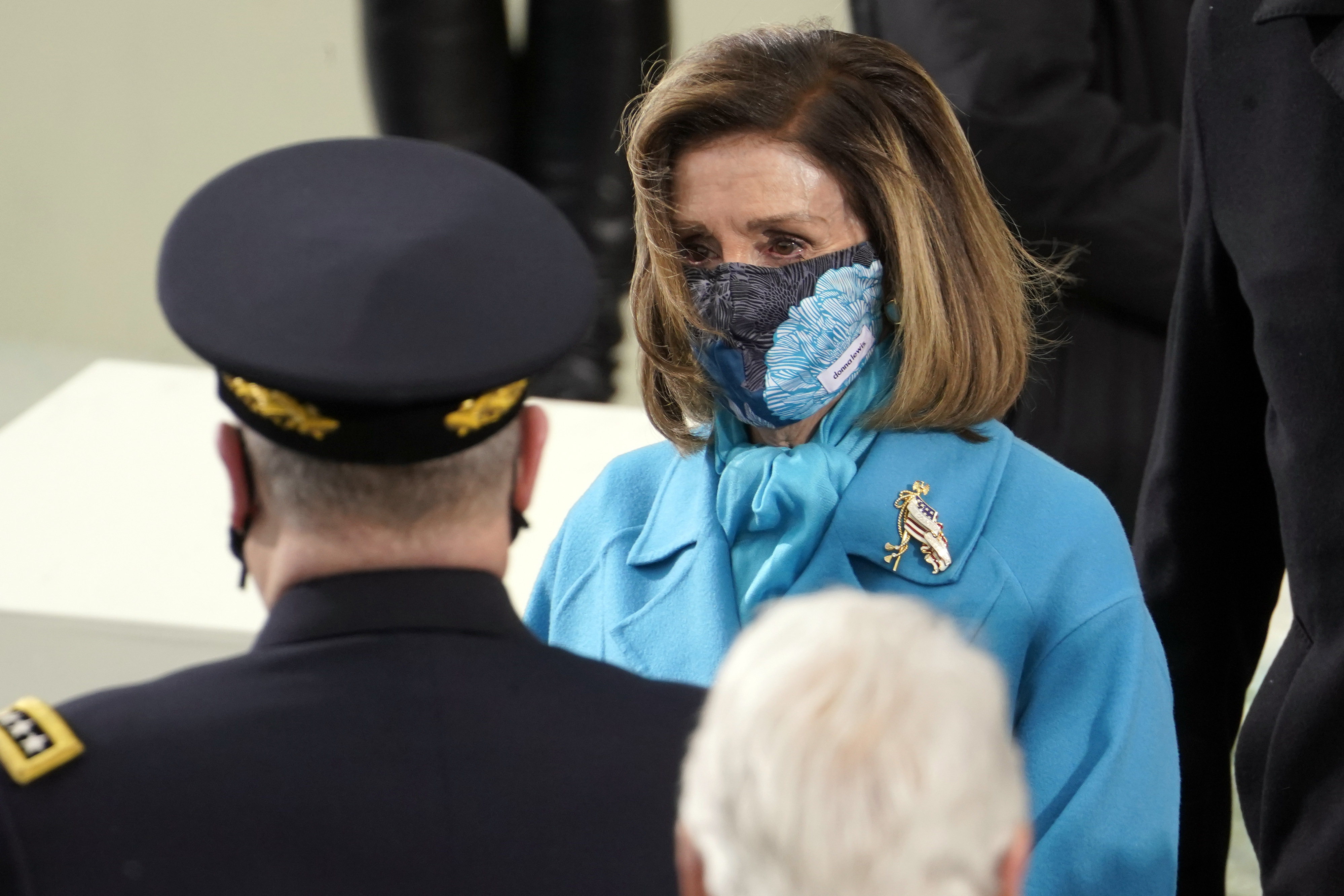 La “speaker” de la Cámara, Nancy Pelosi fue otra que seleccionó el azul como el color ideal para la ceremonia. Y, para darle un toque muy personal, no dejó de llevar un llamativo broche dorado y mascarilla estampada. (AP)
