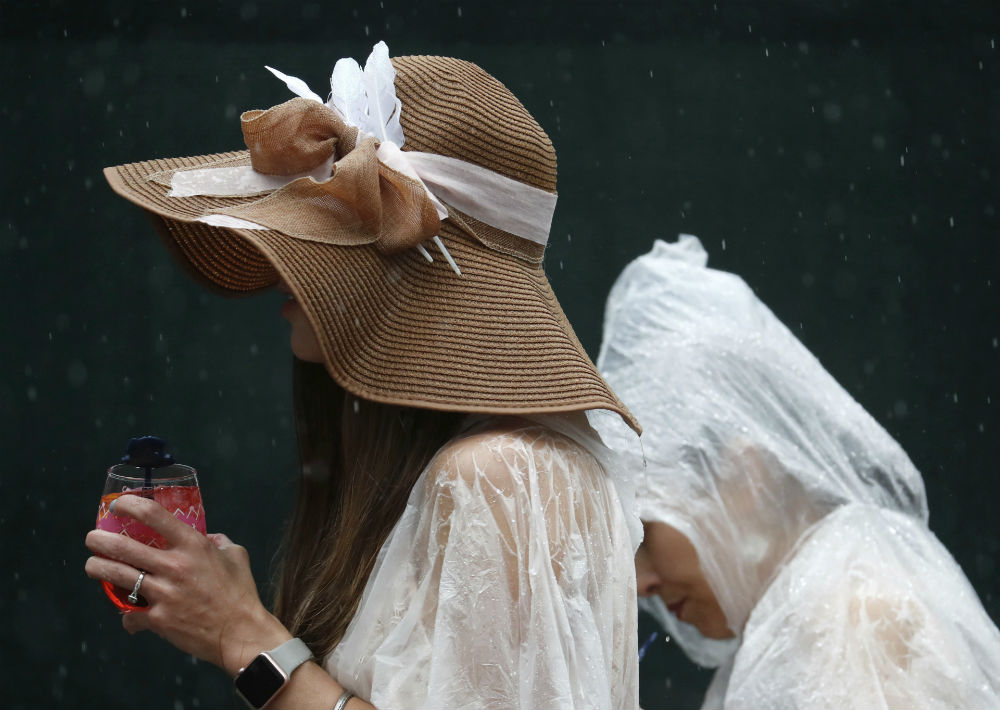 Una mujer camina luciendo una pamela con gran lazo, mientras que otra se protege de la lluvia usando una bolsa plástica sobre su cabeza. (Foto: AP/John Minchillo)