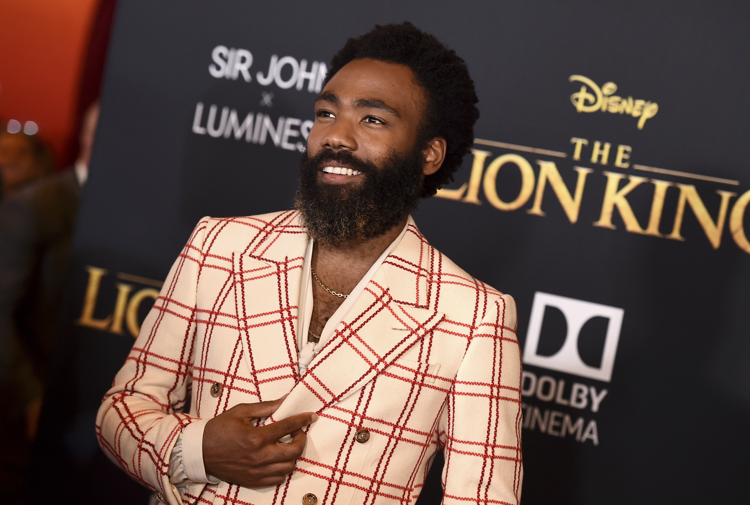Donald Glover, quien le da voz a Simba se presentó en Los Ángeles con un traje claro de Gucci con cuadros rojos y la camisa abierta. (AP)