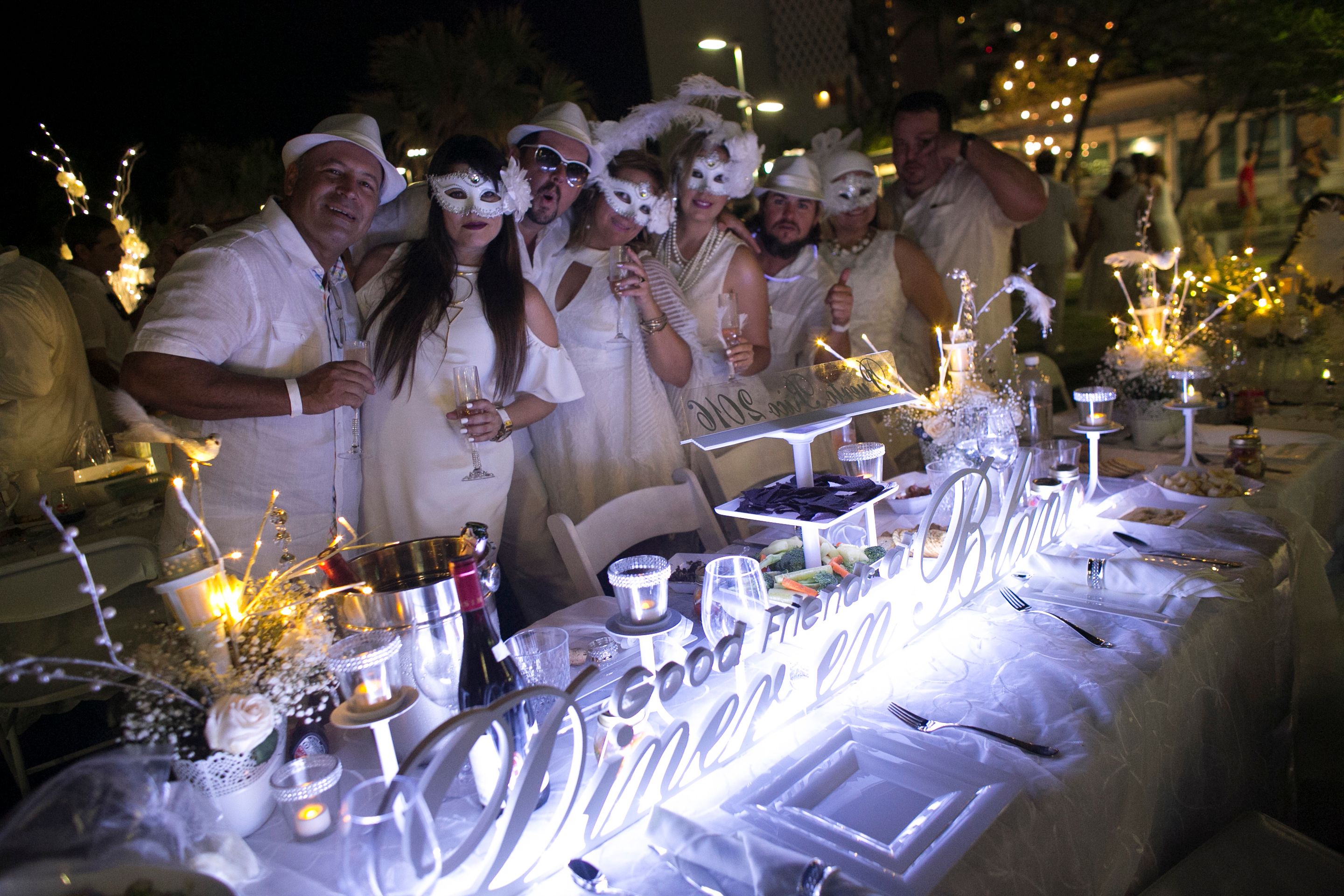 Grupo de invitados -las damas con máscaras de carnaval- lució su espacio con un gran centro de mesa que leía: Good Friends at Dîner en Blanc San Juan.